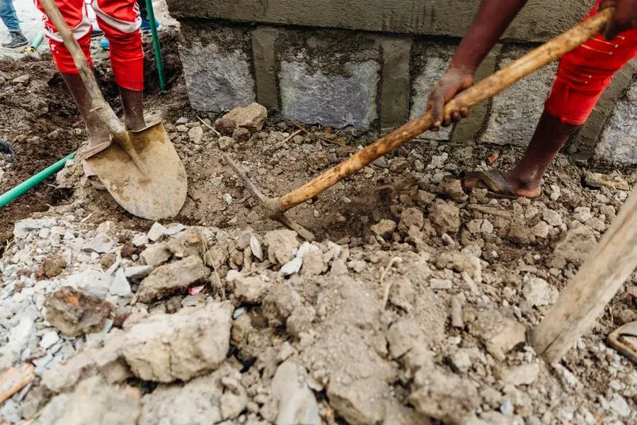 Workers digging through soil to reach a buried pipe